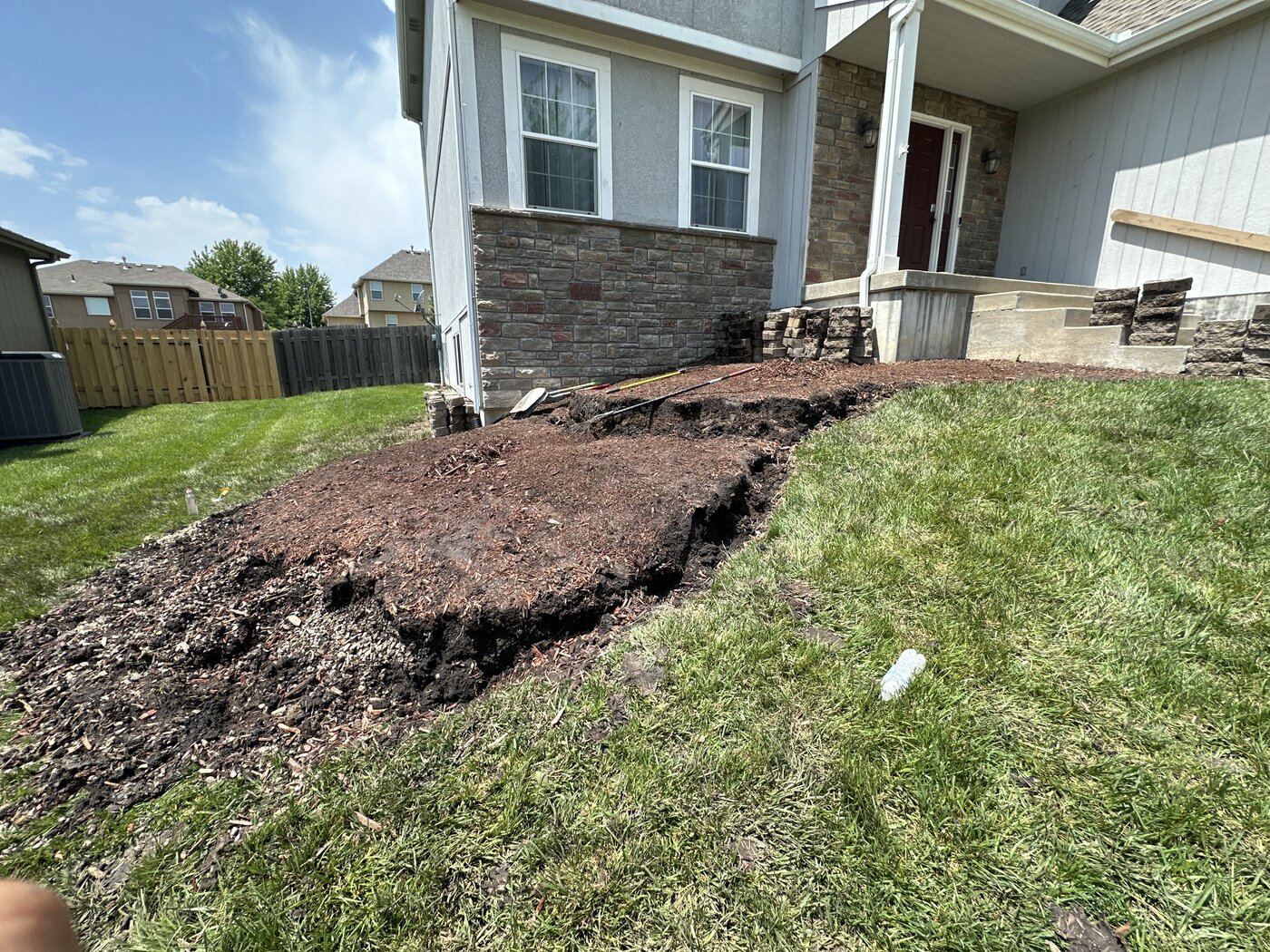 Before: Eroded dirt slope and bare soil right next to the house foundation, with tools and old blocks visible
